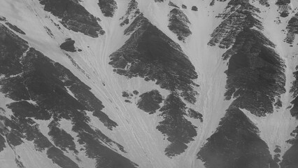 Aerial view of rugged mountain terrain showcasing dramatic snow-covered slopes and rocky outcrops,...