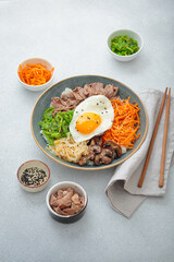 Bibimbap, authentic korean dish with a steamed rice topped with fried egg, beef, colorful vegetables, traditional dish of Korea on light background with chopsticks