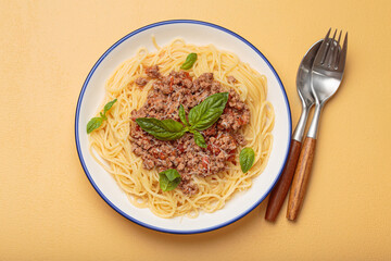 Delicious spaghetti bolognese garnished with fresh basil and grated parmesan, served on a white plate with blue rim, traditional Italian pasta