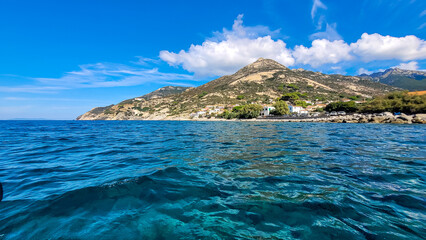 Obraz premium The picturesque coast of the Mediterranean Elba Island and the town of Pomonte on a sunny day. In the foreground is a deep blue sea.