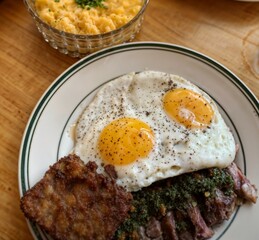 Delicious breakfast plate with sunny side up eggs, fried meat, and macaroni cheese on wooden table