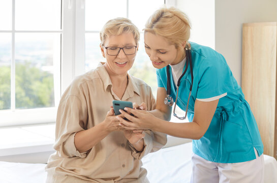 Nurse or caregiver helping elderly woman with usage of smartphone, downloading app for monitoring health, posing in clinic or health centre. Professional guidance and health care concept