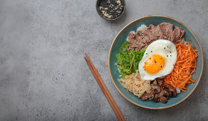Bibimbap, authentic korean dish with a steamed rice topped with fried egg, beef, colorful vegetables, traditional dish of Korea top view on grey background