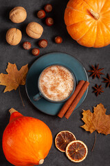 Hot latte in a blue mug, surrounded by autumn leaves, cinnamon sticks, pumpkins, nuts, and dried oranges.