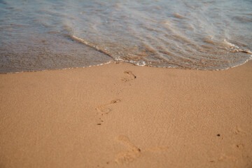 Footprints slowly disappearing beneath gentle ocean waves washing over the sandy beach, creating a tranquil scene that captures the essence of impermanence and solitude