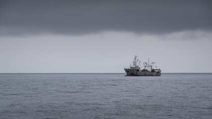 Fishing vessel anchored in calm waters under a dramatic cloudy sky, showcasing the serene maritime environment and the beauty of nature's elements © Denis Tuev