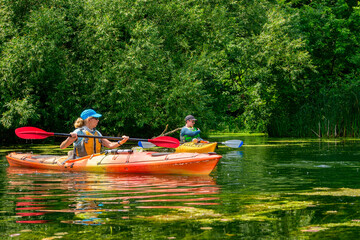 Women paddling sea kayaks on a pong in the Toronto Islands on a summer day with lush green...