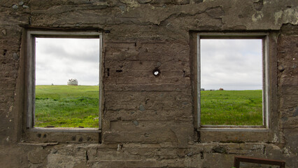 Two empty window frames in a rustic stone wall reveal a lush green landscape outside, showcasing a serene view of nature and inviting a sense of tranquility and openness
