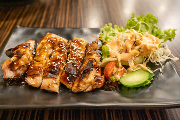 Delicious Grilled Teriyaki Chicken with Fresh Salad on Black Plate at Restaurant