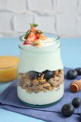Tasty yogurt with granola, berries and honey on light blue table, closeup