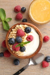 Tasty yogurt with granola, honey and berries in bowl on wooden table, flat lay
