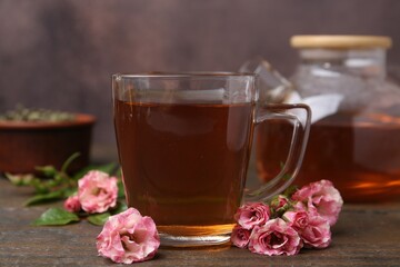 Tasty rose tea in glass cup and flowers on wooden table against brown background, closeup