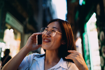 Mid-adult Asian woman reading messages on smartphone in vibrant city environment, showcasing mobile workflow, tech-driven independence, and modern communication culture.