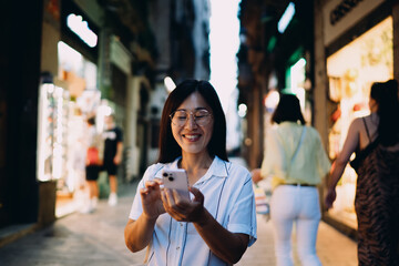 Asian freelancer interacting with smartphone while walking down city street, illustrating seamless...