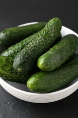 Fresh cucumbers in bowl on dark textured table, closeup
