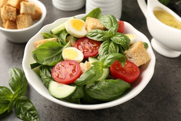 Tasty salad with croutons, tomatoes, cucumbers and basil on black table, closeup
