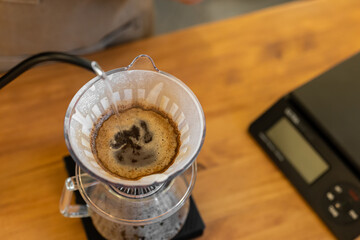 A coffee dripper sits on a scale, with freshly brewed coffee dripping into a glass carafe. The...