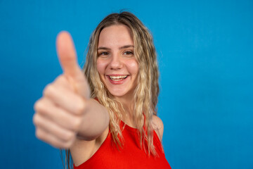 Young woman showing thumb up sign and smiling on blue background