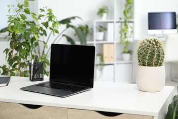 Stylish workplace with laptop, stationery and floral decor in office. Biophilic interior design