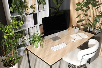 Stylish workplace with modern computer, stationery and floral decor in office. Biophilic interior design