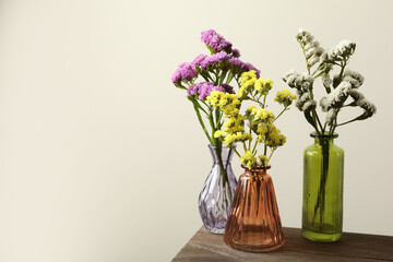 Beautiful flowers in glass vases on wooden table against beige background, space for text