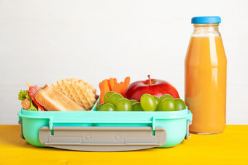 Open lunch box with delicious food and juice on yellow wooden table against light grey background, closeup