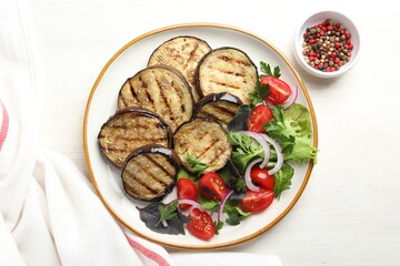 Grilled slices of eggplant with salad and peppercorns on white wooden table, top view