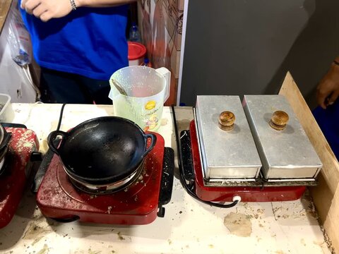 A food vendor is cooking kue cubit or a sweet pancake, on a frying pan. Kue cubit is a Betawi Indonesian specialty. It's made from flour, milk, and chocolate sprinkles