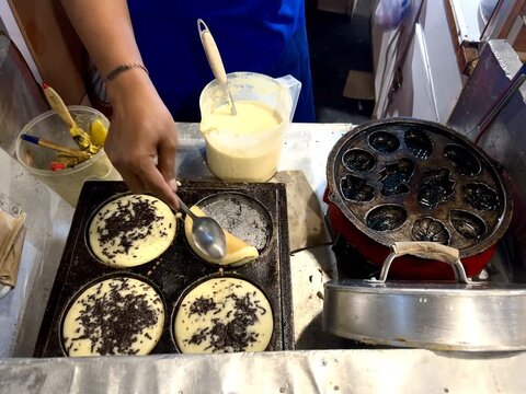 A food vendor is cooking kue cubit or a sweet pancake, on a frying pan. Kue cubit is a Betawi Indonesian specialty. It's made from flour, milk, and chocolate sprinkles