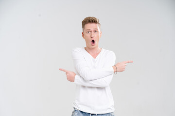 Young Caucasian man displays a surprised expression while pointing with both hands against a plain white background. His astonished demeanor captures a moment of excitement and wonder.
