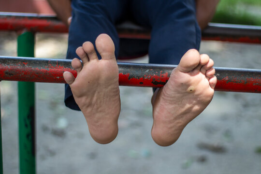 A persons bare feet dangle from a metal bar at a park - Powered by Adobe