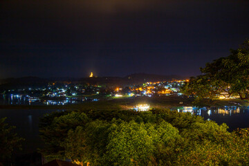 Burmese-influenced temple pagoda emerging from the tree line on a mountain with the river view, on a misty day. Kanchanaburiม Thailand.
