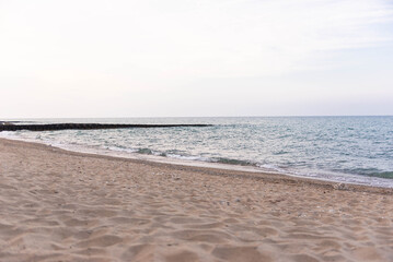 Sandy beach with sea waves and breakwater