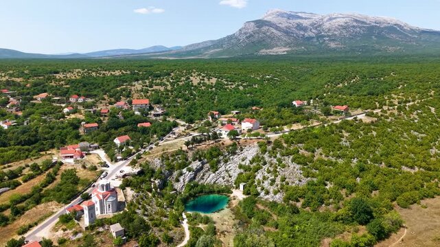 Drone panorama over Cetina River spring near Vrlika Croatia turquoise karst eye beside medieval Holy Salvation church