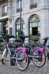 Fototapeta premium A cityscape of Besançon, France, featuring rental bicycles in the foreground with urban buildings and streets in the background, capturing everyday urban life.