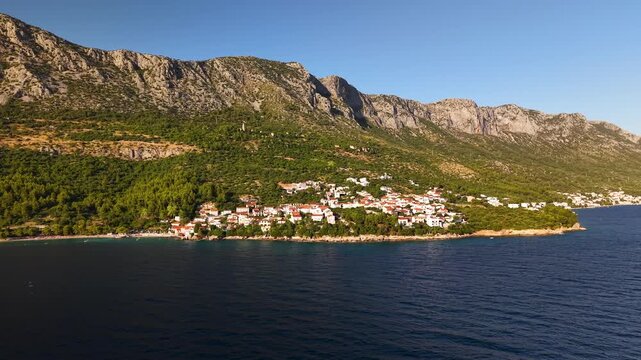 Golden hour drone panorama of Igrane village beneath Biokovo cliffs along the Makarska Riviera Adriatic coastline