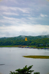 Burmese-influenced temple pagoda emerging from the tree line on a mountain with the river view, on a misty day. Kanchanaburiม Thailand.