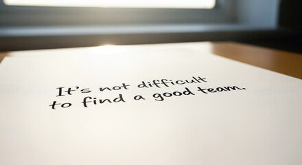 Its not difficult to find a good team Inspirational quote handwritten on a piece of paper placed on a wooden table near a window with sunlight coming through
