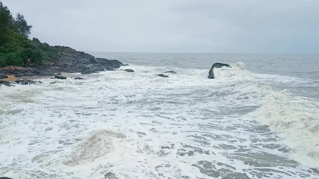 footage of ocean waves gently crashing against tetrapod rock barriers on a serene beach. Ideal for background, nature, travel, or environmental themes with calm sea and sandy shoreline.