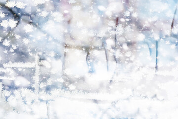 Winter landscape through a frozen window. Blurred snow background. Trees and plants covered with...