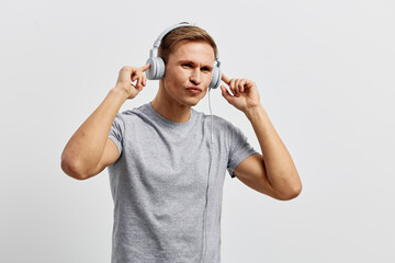 Young man wearing casual gray t-shirt listening to music through large headphones against plain...