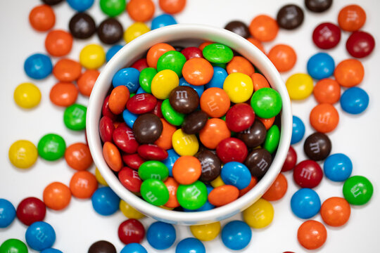 a bowl of colorful bright mms milk chocolate candies on white background with candy spills