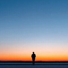 Obraz premium Solitary silhouette of person stands against vibrant sunset horizon, evoking sense of calm and introspection. expansive sky transitions from deep blue to warm orange hues