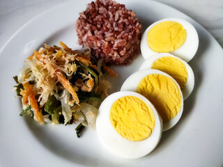 Red rice with vegetable salad or gudangan and a boiled egg on a white plate. A healthy meal concept.