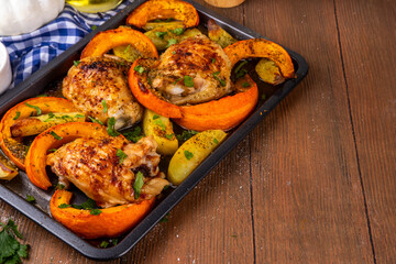 Roasted baked chicken thigh with pumpkin and potato wedges, garlic and aromatic herbs. Tasty autumn comfort food, ideas for Thanksgiving family dinner