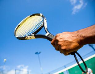 Tennis Racket Held Against Blue Sky, Close-Up of Hand and Equipment, Outdoor Sport