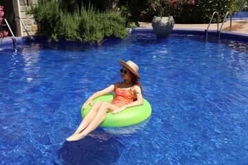 Girl on inflatable ring in swimming pool outdoors on sunny day