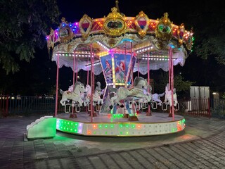 Carousel ride with decorative horses in an amusement park at night. Traditional fairground...