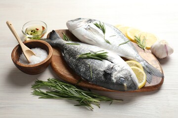 Fresh raw dorado fish, lemon slices, rosemary and spices on white wooden table, closeup. Organic...