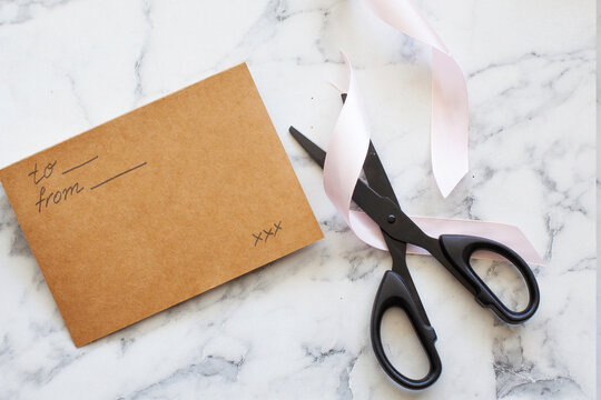 Top view of black scissors, greeting card and pink satin ribbon on marble background